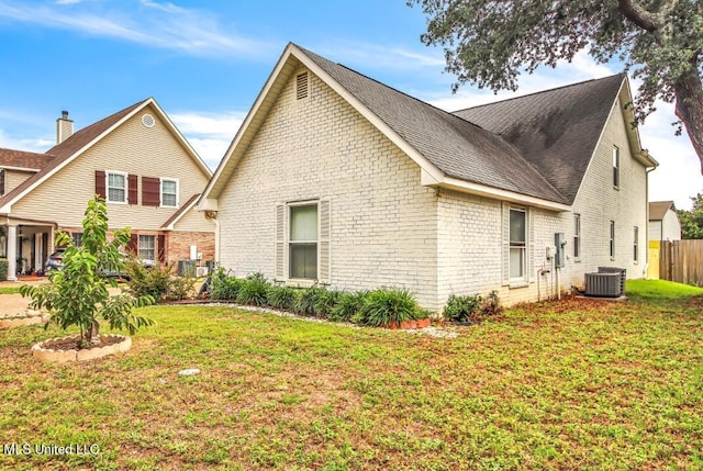 view of side of property with brick siding, a lawn, cooling unit, and fence