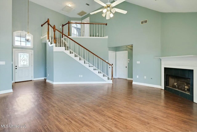 unfurnished living room featuring wood finished floors, visible vents, baseboards, stairs, and a tiled fireplace