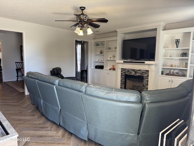 living area with a textured ceiling, a ceiling fan, crown molding, and a stone fireplace