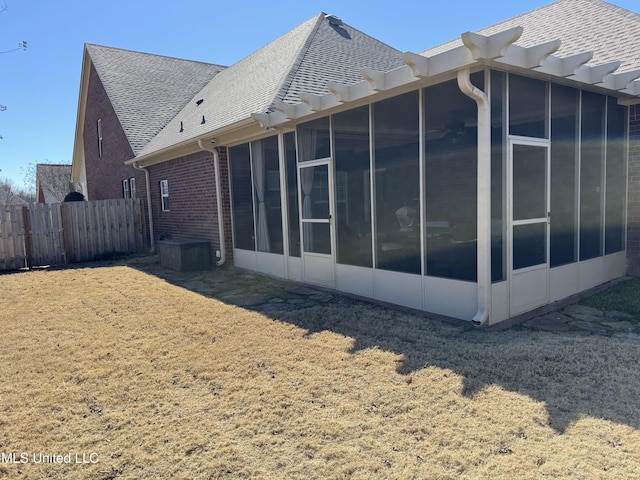 view of side of property with brick siding, a yard, a shingled roof, a sunroom, and fence