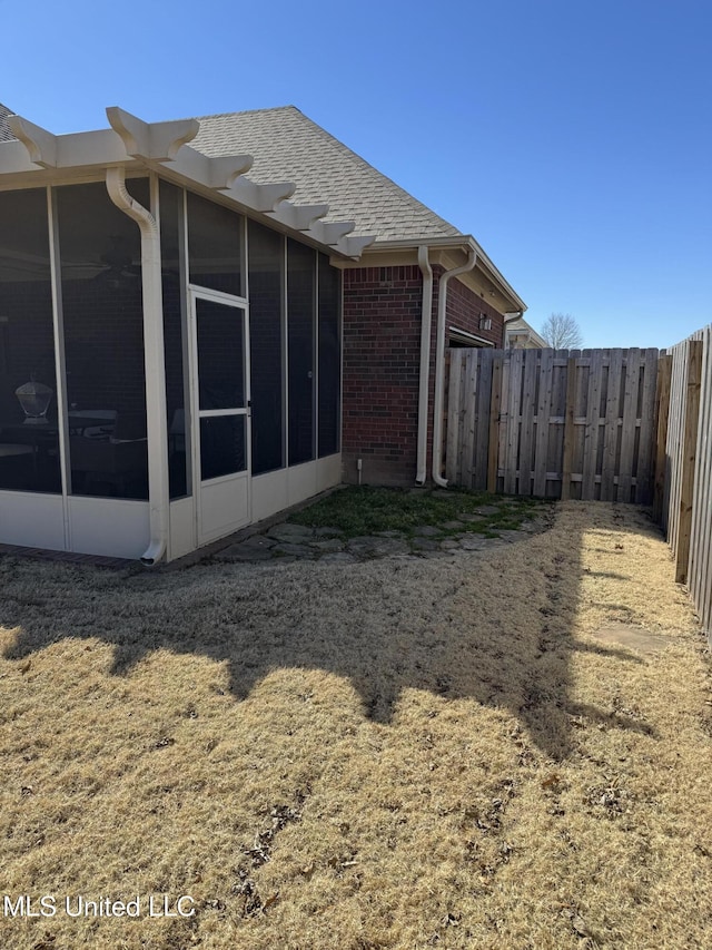 view of side of property with brick siding, roof with shingles, a fenced backyard, and a sunroom