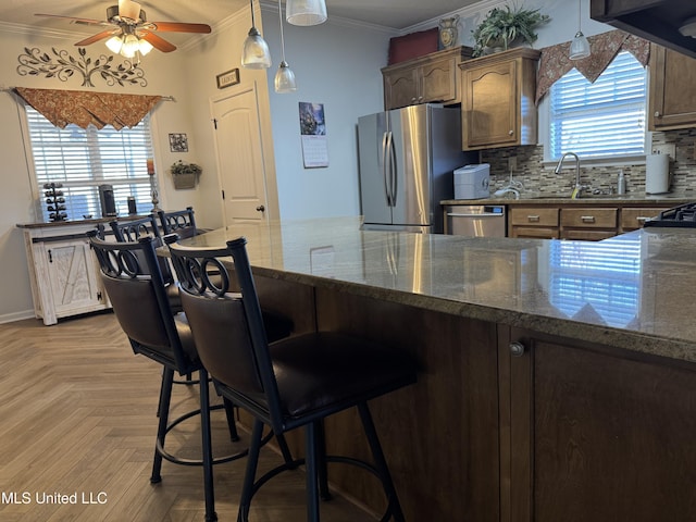 kitchen with tasteful backsplash, appliances with stainless steel finishes, ornamental molding, a sink, and dark stone countertops