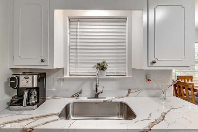 kitchen featuring light stone counters, sink, and white cabinets