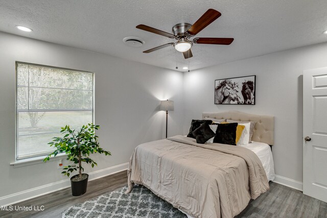 bedroom with a textured ceiling, ceiling fan, dark wood-type flooring, and multiple windows