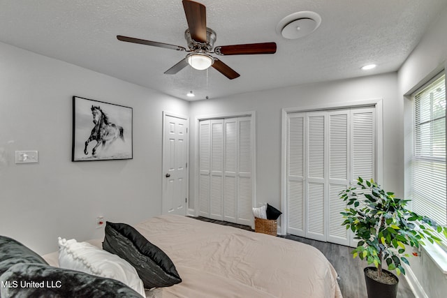 bedroom with a textured ceiling, ceiling fan, two closets, and hardwood / wood-style flooring