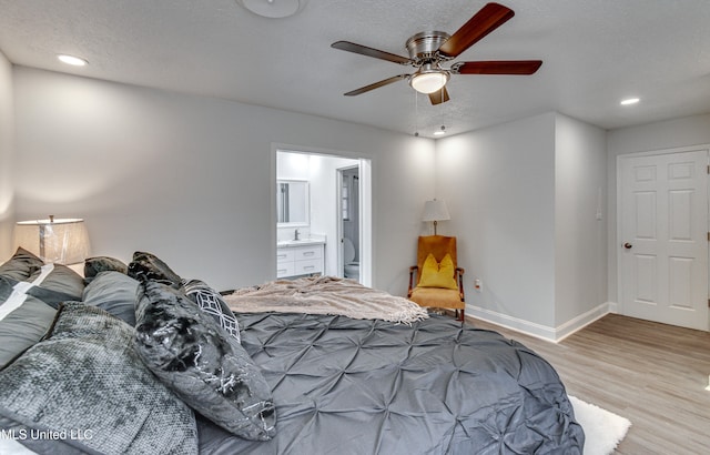 bedroom with ceiling fan, light hardwood / wood-style floors, a textured ceiling, and connected bathroom