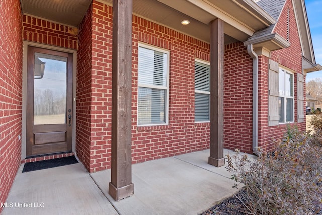 doorway to property featuring brick siding, a porch, and a shingled roof