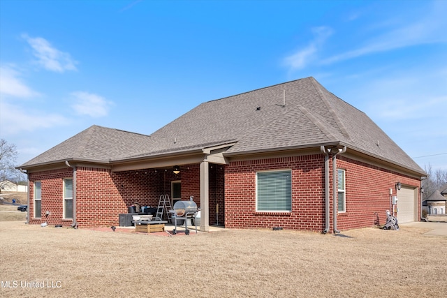 rear view of property featuring roof with shingles, brick siding, a lawn, an attached garage, and a patio area