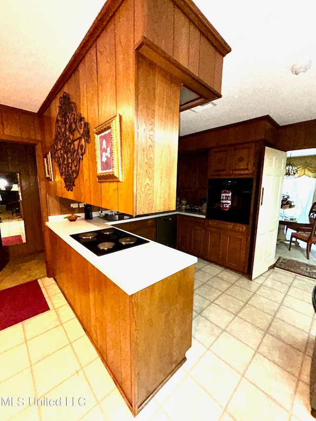 kitchen featuring black appliances, kitchen peninsula, wooden walls, ornamental molding, and light tile patterned floors