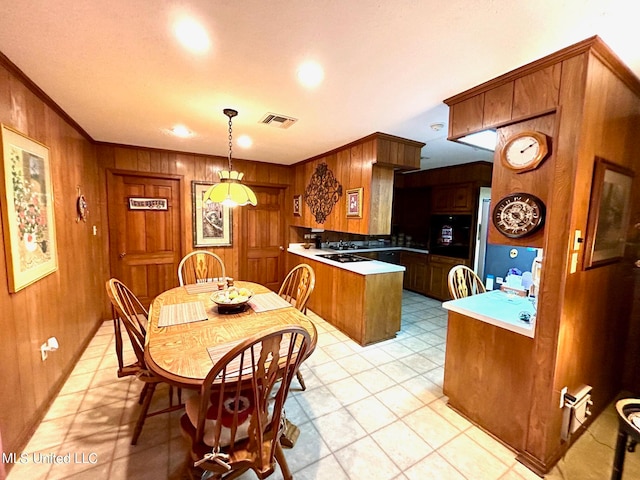 kitchen featuring kitchen peninsula, hanging light fixtures, ornamental molding, light tile patterned floors, and wood walls