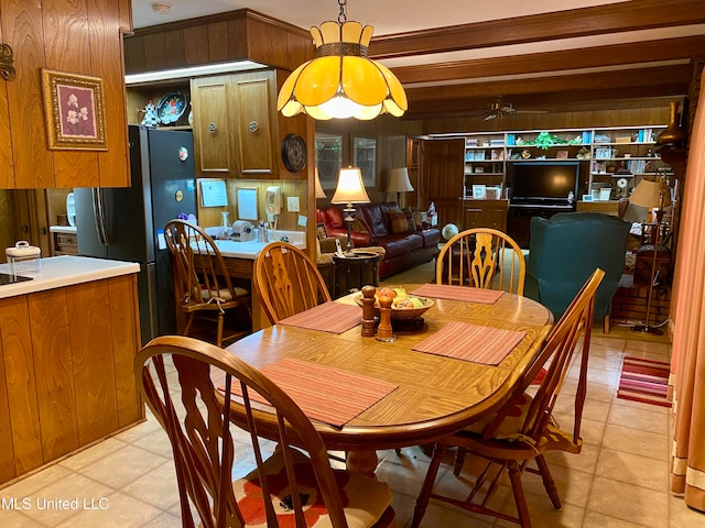 dining room with beamed ceiling, wooden walls, ceiling fan, and light tile patterned floors