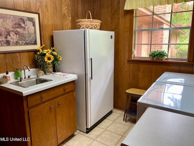 kitchen featuring sink, separate washer and dryer, light tile patterned floors, white fridge, and wood walls