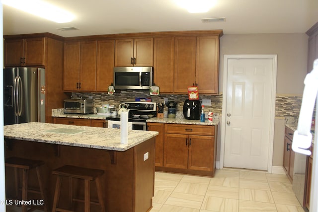 kitchen featuring backsplash, a center island, light stone countertops, and stainless steel appliances