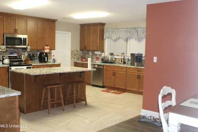 kitchen with decorative backsplash, appliances with stainless steel finishes, a kitchen island, and light stone counters