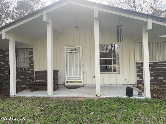 entrance to property featuring brick siding, board and batten siding, and a patio area