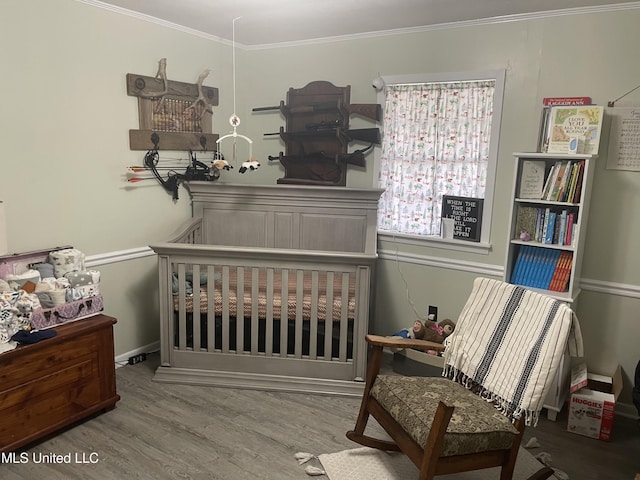 bedroom with a crib, crown molding, and wood finished floors