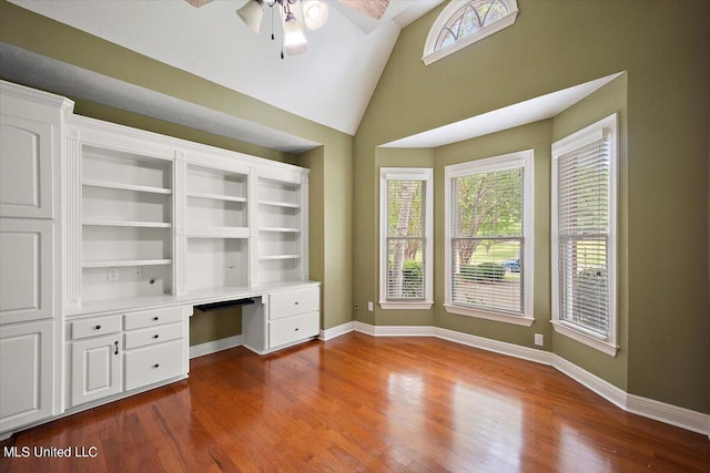 unfurnished office with a ceiling fan, baseboards, built in desk, and dark wood-type flooring