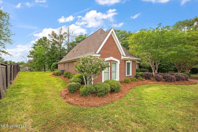 view of side of home with brick siding, roof with shingles, fence, and a yard