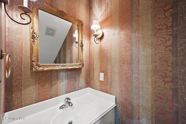 bathroom with visible vents, vanity, and wallpapered walls