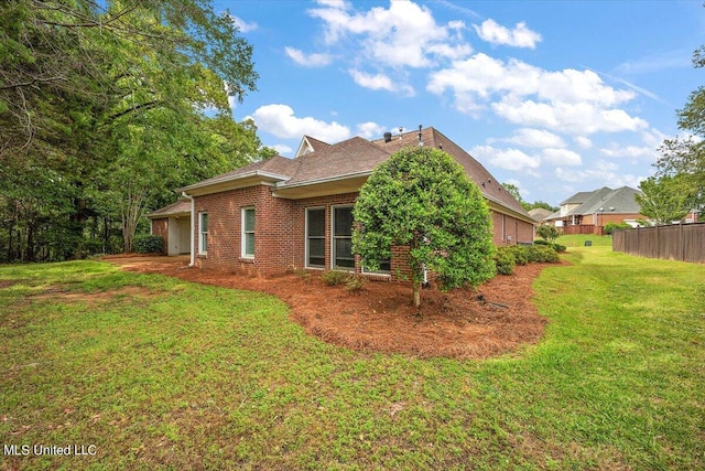 view of side of property featuring brick siding, a lawn, and fence