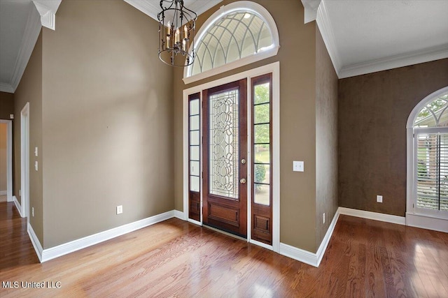 foyer featuring baseboards, ornamental molding, wood finished floors, and a chandelier