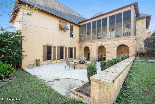 back of house with a lawn, an outdoor fire pit, a patio area, and a sunroom