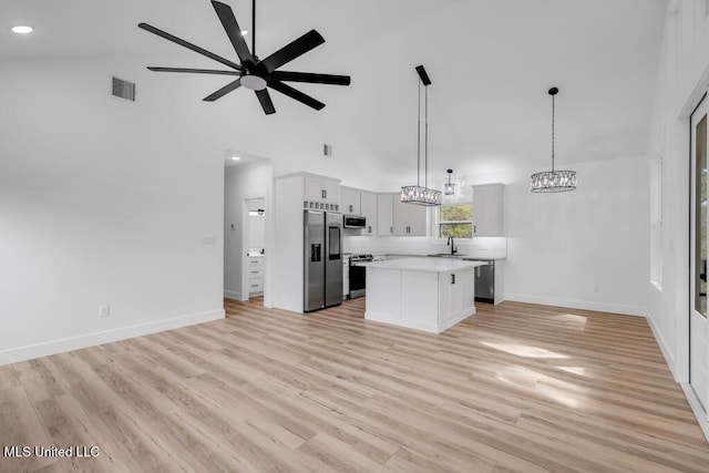 kitchen featuring a kitchen island, open floor plan, light countertops, appliances with stainless steel finishes, and decorative light fixtures