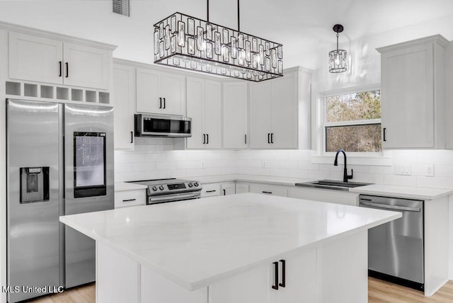 kitchen with stainless steel appliances, white cabinetry, a kitchen island, and decorative light fixtures