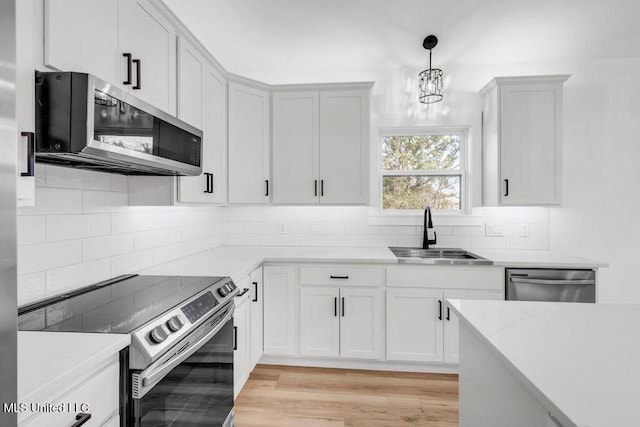 kitchen featuring hanging light fixtures, light stone countertops, stainless steel appliances, white cabinetry, and a sink