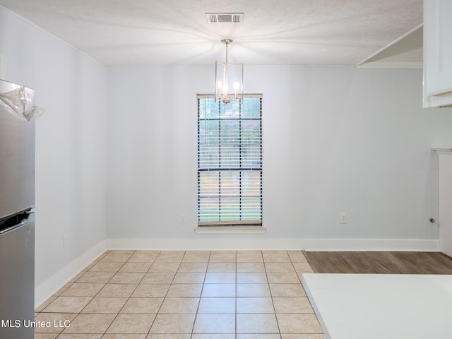 unfurnished dining area featuring an inviting chandelier, a textured ceiling, and light tile patterned flooring