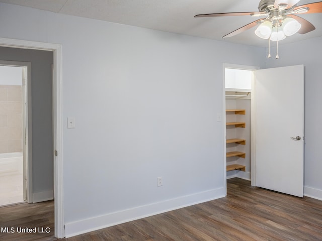 unfurnished bedroom featuring dark wood-type flooring, ceiling fan, a closet, and a walk in closet