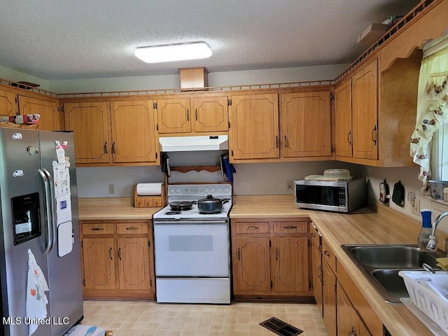 kitchen with appliances with stainless steel finishes, a sink, light countertops, under cabinet range hood, and visible vents