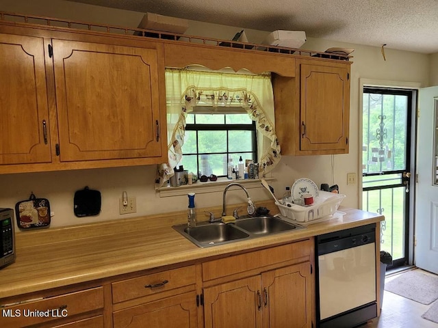 kitchen featuring stainless steel dishwasher, a sink, a textured ceiling, and light countertops