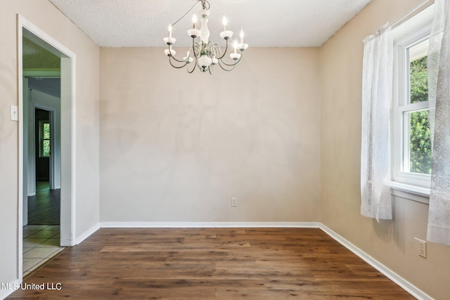 empty room featuring a textured ceiling, a chandelier, and dark hardwood / wood-style floors