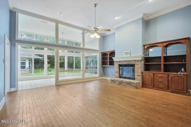 unfurnished living room with ceiling fan, light wood-type flooring, a fireplace, a towering ceiling, and crown molding