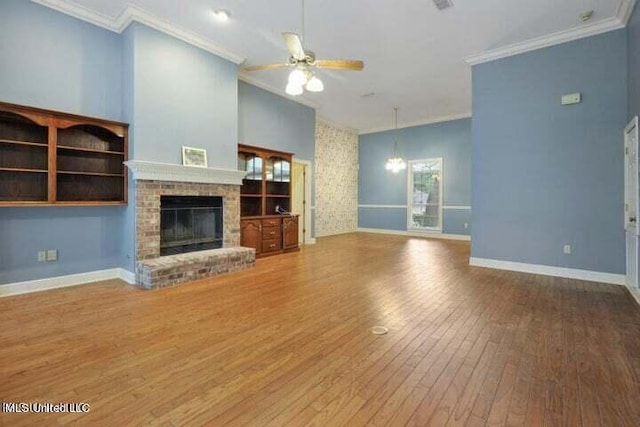 unfurnished living room with crown molding, a fireplace, hardwood / wood-style flooring, and ceiling fan with notable chandelier