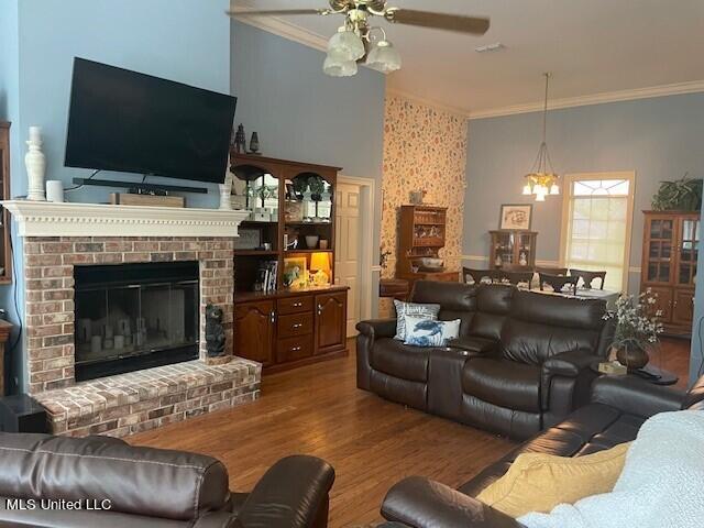 living room featuring crown molding, a brick fireplace, hardwood / wood-style flooring, and ceiling fan with notable chandelier