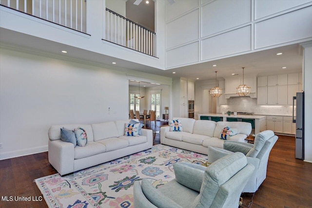 living room with ornamental molding, a high ceiling, an inviting chandelier, and dark hardwood / wood-style flooring