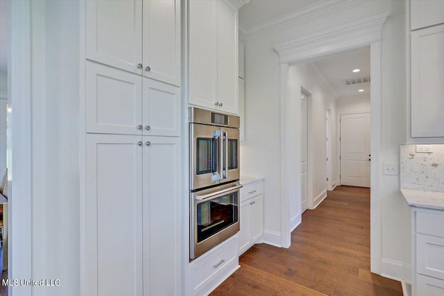 kitchen with light stone countertops, double oven, white cabinets, crown molding, and dark hardwood / wood-style floors