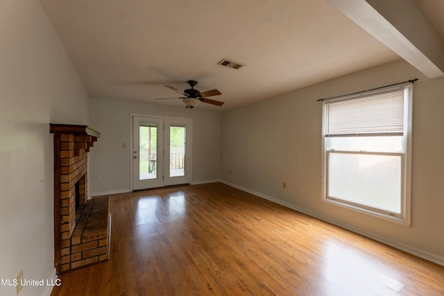 unfurnished living room with a brick fireplace, light wood-type flooring, and ceiling fan