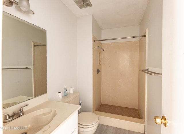 bathroom with vanity, hardwood / wood-style floors, a tile shower, and toilet