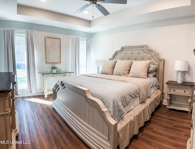 bedroom with dark wood-style floors, a tray ceiling, and baseboards