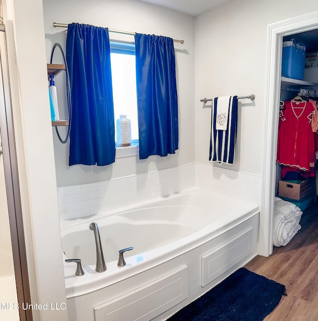 full bathroom featuring wood finished floors, a garden tub, and a walk in closet