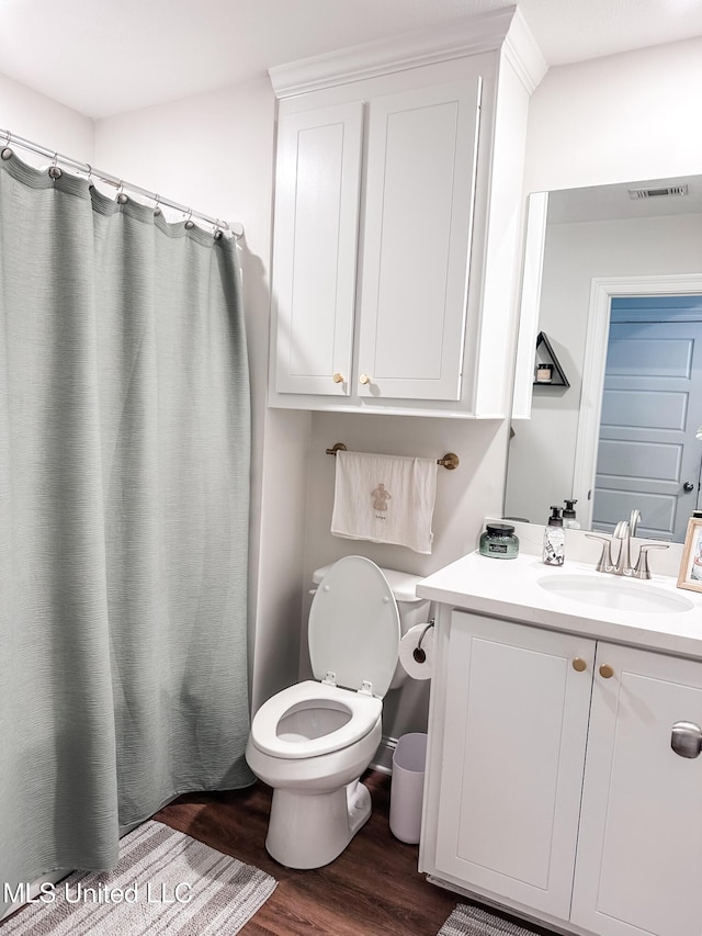 bathroom with toilet, vanity, wood finished floors, and visible vents