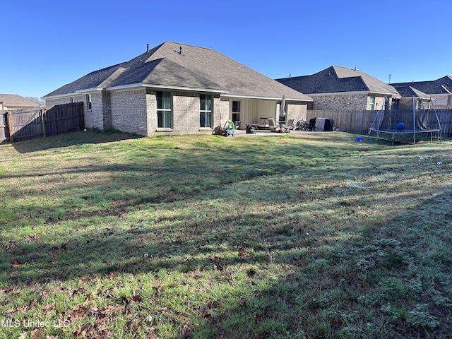 back of property with a trampoline, a patio area, brick siding, and a fenced backyard