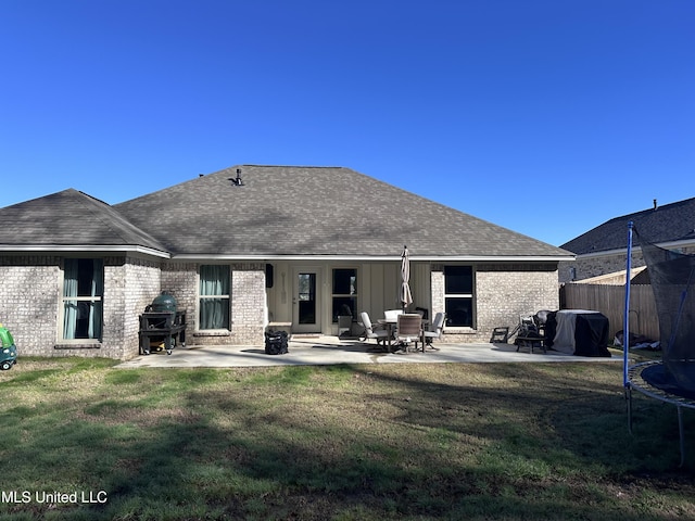 rear view of property with brick siding, a trampoline, and a patio area