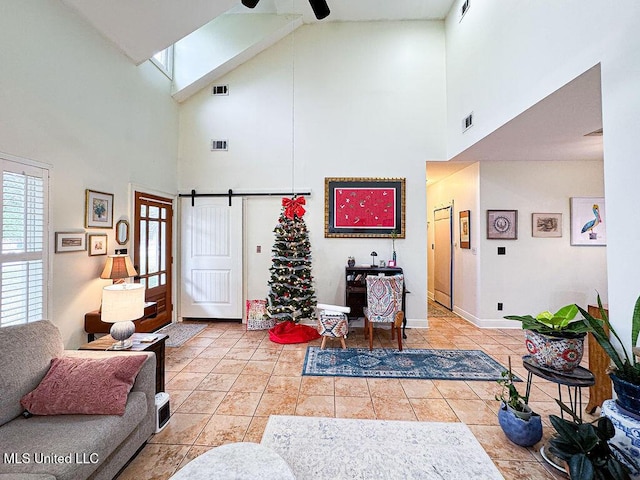 living area featuring ceiling fan, a barn door, light tile patterned flooring, and visible vents