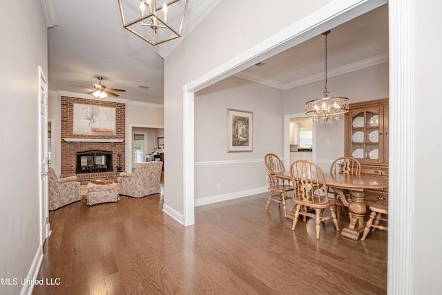 dining area featuring a brick fireplace, ceiling fan with notable chandelier, wood-type flooring, and crown molding