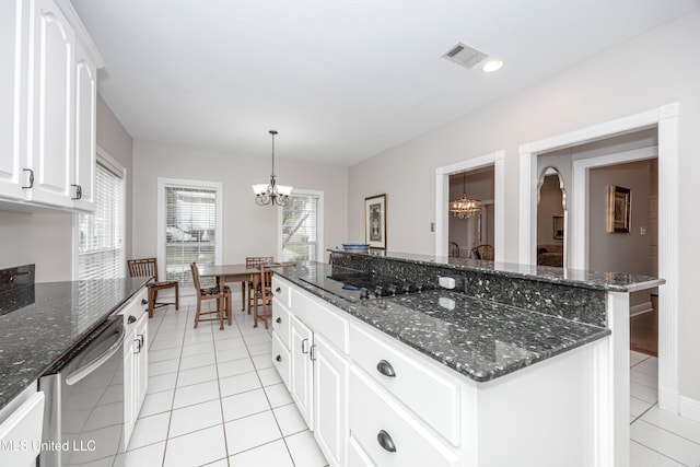 kitchen with dark stone counters, an inviting chandelier, light tile patterned floors, stainless steel dishwasher, and white cabinetry