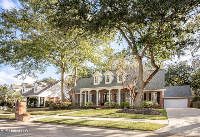 new england style home featuring a front yard, a garage, and covered porch